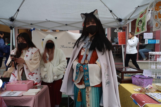 A bustling convention floor with vendors selling cosplay materials like fabrics, wigs, armor pieces, and prop weapons, demonstrating the commercial aspect of the cosplay industry.