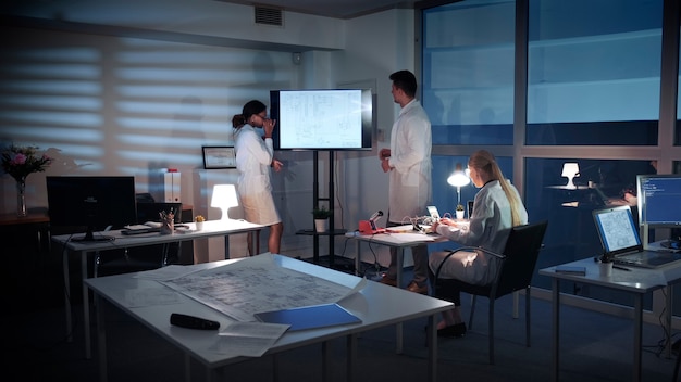 An immersive virtual workspace environment, where remote team members interact as avatars in a simulated office setting. The scene includes interactive whiteboards and 3D project visualizations.