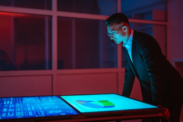 A programmer shown working at a desk, but via hologram. The hologram is displaying a multi-layered code design, a visual representation of AI running.