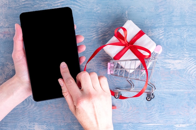 A close-up shot of a person's hands holding a gift card, with a smartphone displaying a coupon code app in the background. The scene suggests combining various savings methods.