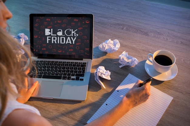 A person sitting at a desk, illuminated by the glow of a laptop screen, surrounded by sale stickers and Black Friday promotional materials.