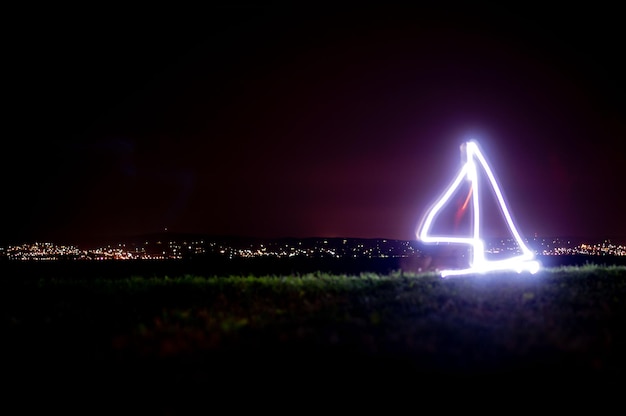 A night vision style photograph showing a series of lights arrayed in a triangular formation against a dark sky. The landscape below is barely visible, suggesting a rural or remote location.