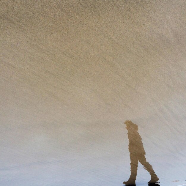 A person walking on a sand dune, with visible ripples and patterns in the sand, illustrating how the disturbance of the sand can create the sound.
