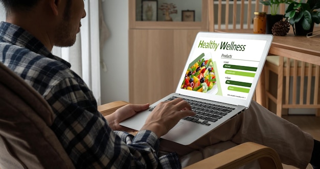 A person browsing an online grocery store website on a laptop, with a shopping cart icon prominent on the screen. A banner at the top of the website advertises a 15% off discount on first-time orders. The overall setting is a cozy home environment, with a cup of coffee next to the laptop.
